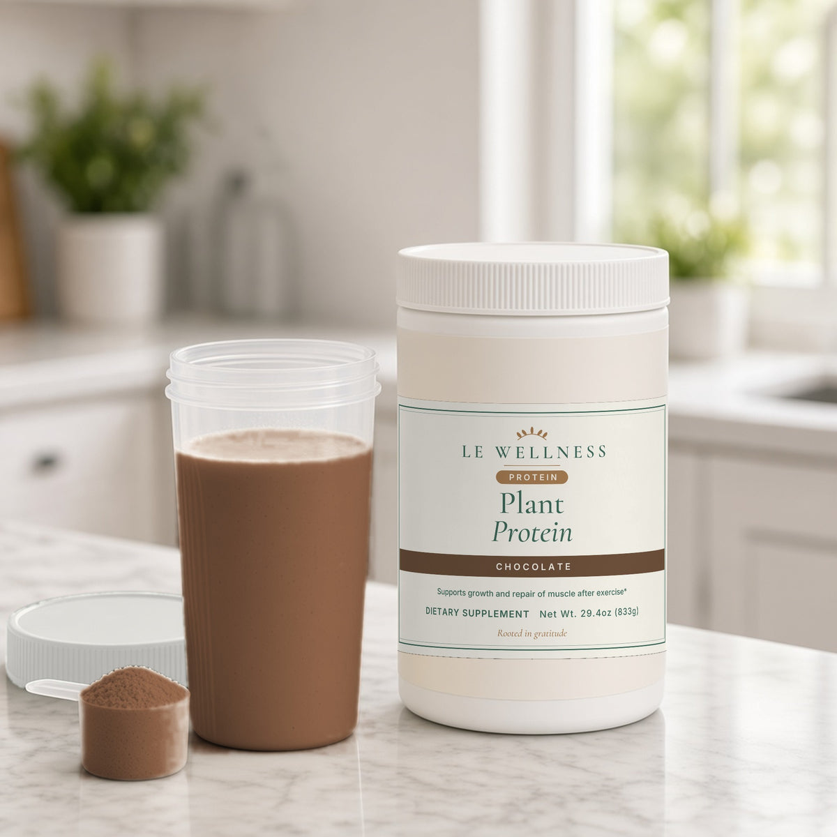 Le Wellness Plant Protein (Chocolate) tub on a marble kitchen counter with a chocolate protein shake and scoop